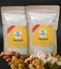 Two pouches of homemade talbina original (1.2kg) with a yellow label, surrounded by an assortment of dry fruits and nuts like almonds, cashews, and raisins. The pouches are labeled 'Talbina' and feature a natural, wholesome look, perfect for preparing the nourishing barley-based dish.