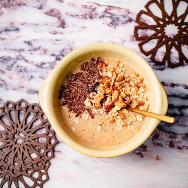 Talbina bowl topped with chocolate shavings, granola, and nuts in a ceramic bowl on a marble surface